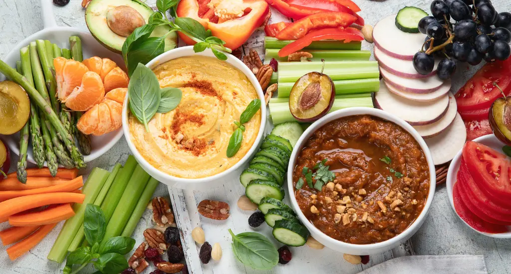 Healthy vegan snack ideas and dips. Flatlay of party food. Top view on gray background. Clean diet eating, veggie serving table